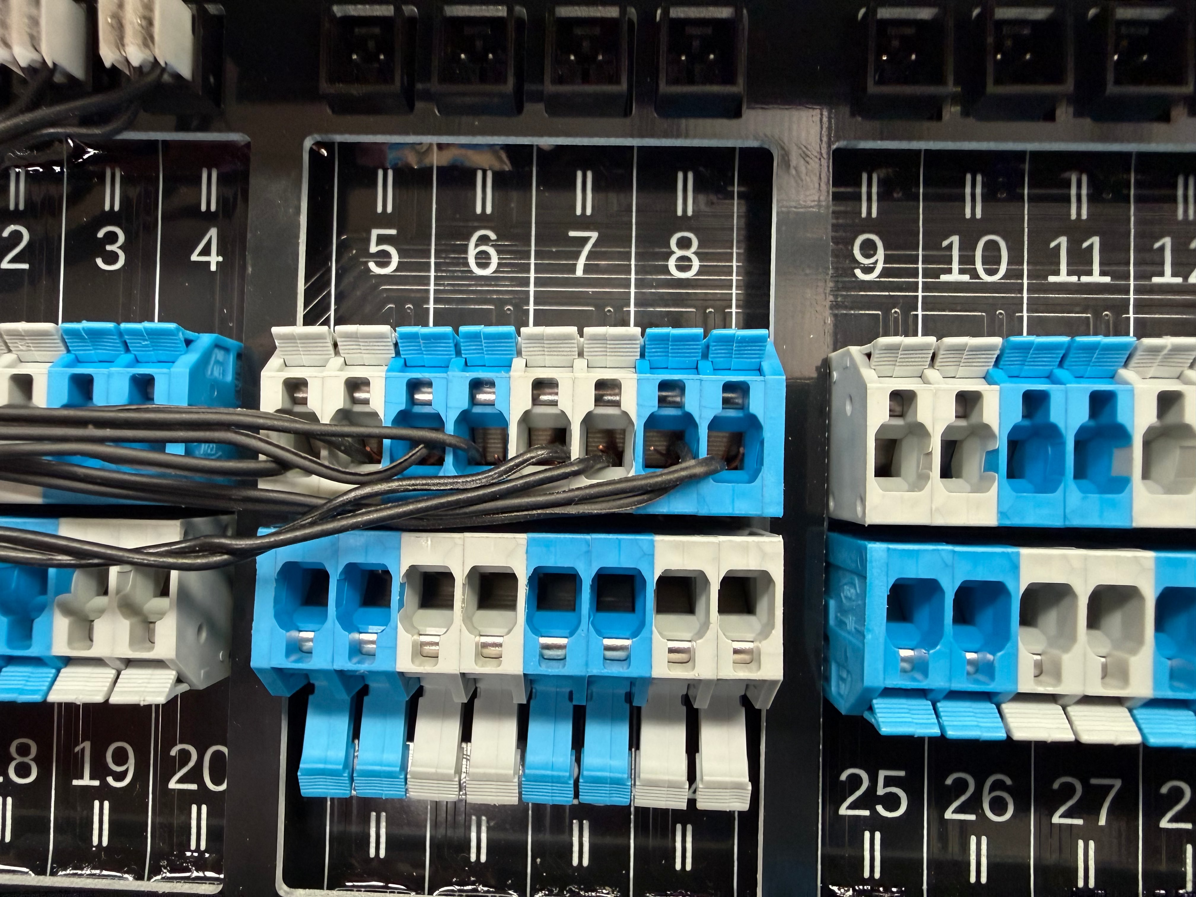 Close-up of blue and white electrical terminal blocks connected to black power cords on a control panel.
